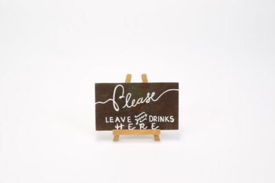 Dark wooden sign- "Please leave your drinks here"